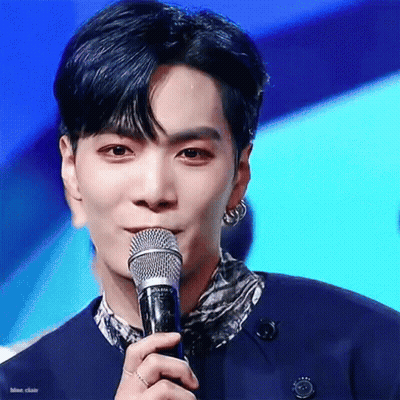 A Young Man Is Holding A Microphone In His Hand And Talking Into It . GIF