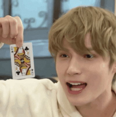 A Young Man Is Holding A Playing Card In His Hand And Pointing It At The Camera . GIF