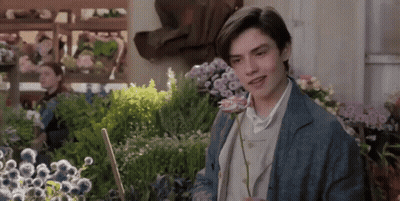 A Young Man Is Holding A Rose In A Garden GIF