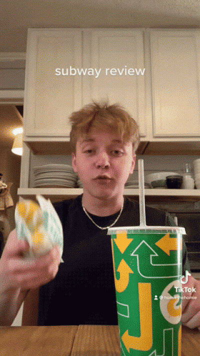 A Young Man Is Holding A Sandwich And A Subway Cup GIF