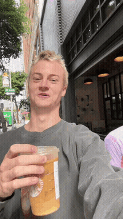 A Young Man Is Holding A Starbucks Cup In Front Of A Building GIF