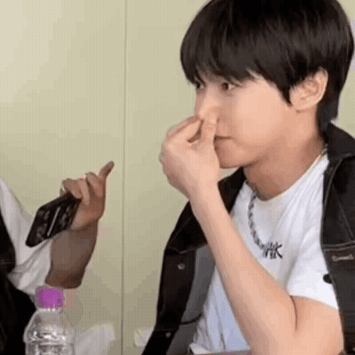 A Young Man Is Holding His Nose While Sitting At A Table With A Bottle Of Water . GIF
