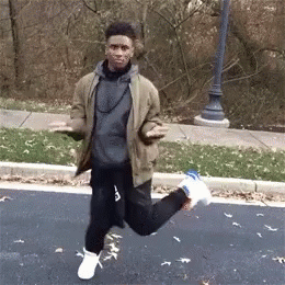 A Young Man Is Jumping In The Air While Standing On The Side Of The Road . GIF