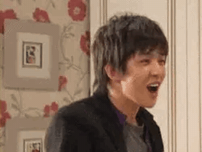 A Young Man Is Laughing With His Mouth Open In A Room With Pictures On The Wall . GIF