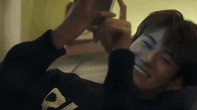 A Young Man Is Laying On A Bed Taking A Selfie With His Phone . GIF