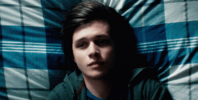 A Young Man Is Laying On A Bed With A Blue And White Plaid Blanket GIF
