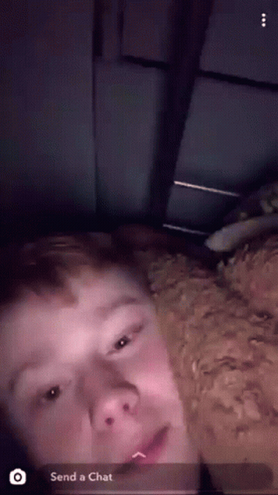 A Young Man Is Laying On A Bed With A Dog And A Snapchat Message That Says " Send A Chat " GIF