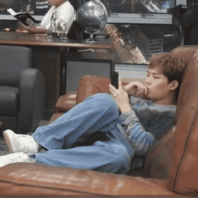 A Young Man Is Laying On A Couch Looking At His Phone GIF