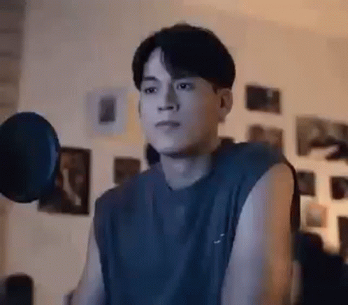 A Young Man Is Lifting A Dumbbell In A Room . GIF
