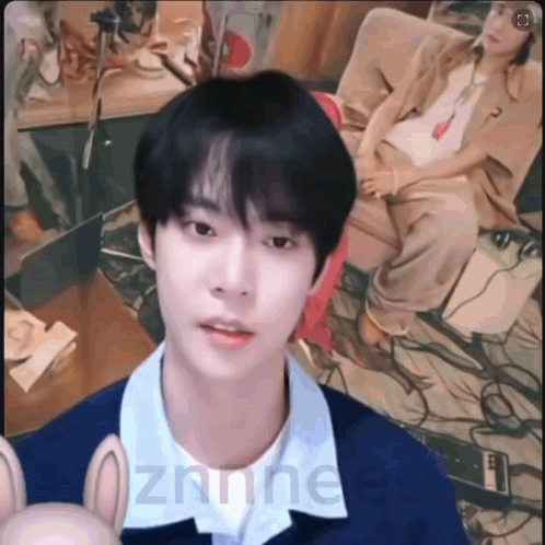 A Young Man Is Looking At The Camera While A Woman Sits Behind Him On A Couch . GIF