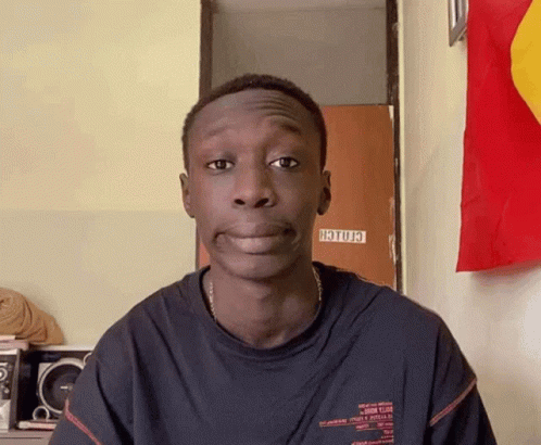 A Young Man Is Making A Funny Face In Front Of A Wall With A Sign That Says ' Hotu3 ' On It GIF