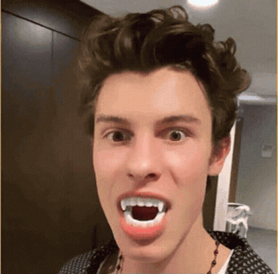 A Young Man Is Making A Funny Face With Fake Vampire Teeth . GIF