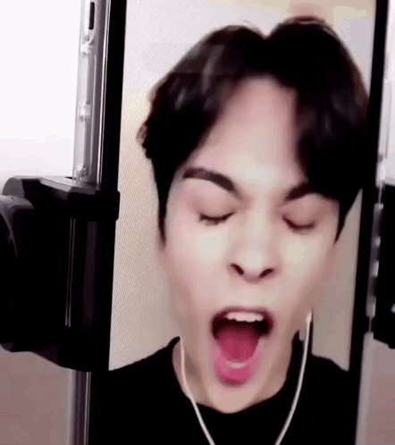 A Young Man Is Making A Funny Face With His Mouth Open While Wearing Earphones . GIF