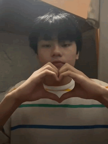 A Young Man Is Making A Heart Shape With His Hands And Hearts Are Coming Out Of His Eyes GIF