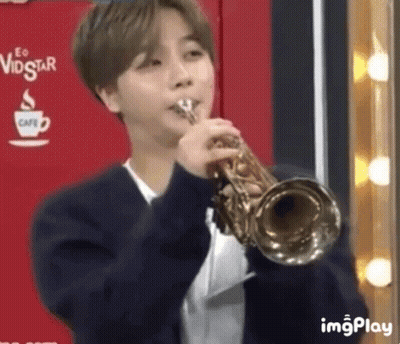 A Young Man Is Playing A Trumpet In A Room . GIF