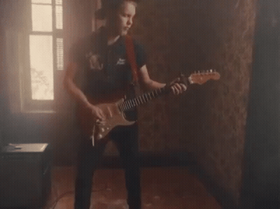 A Young Man Is Playing An Electric Guitar In A Dark Room . GIF