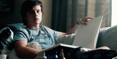 A Young Man Is Reading A Book While Laying On A Couch . GIF