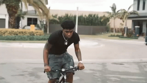 A Young Man Is Riding A Bicycle Down A Street . GIF