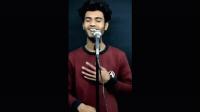 A Young Man Is Singing Into A Microphone While Holding His Hand To His Chest . GIF