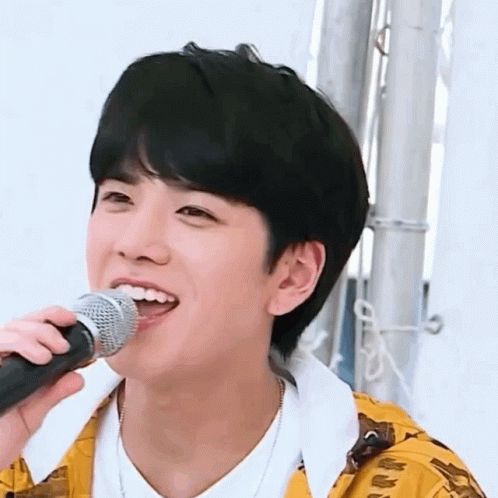A Young Man Is Singing Into A Microphone While Wearing A Yellow Jacket . GIF
