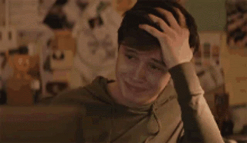 A Young Man Is Sitting At A Desk Holding His Head . GIF