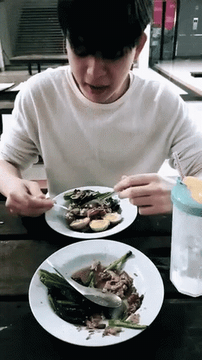 A Young Man Is Sitting At A Table Eating A Plate Of Food GIF
