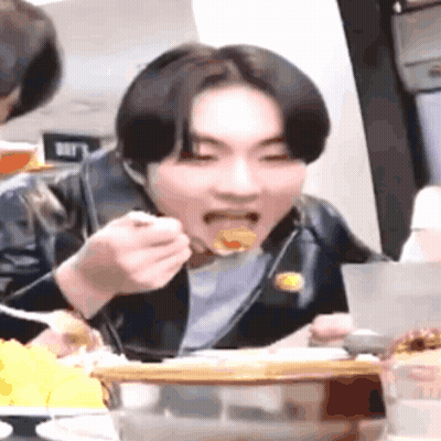 A Young Man Is Sitting At A Table Eating Food With A Fork And Spoon . GIF