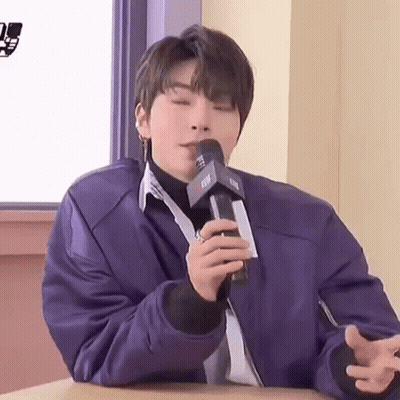 A Young Man Is Sitting At A Table Holding A Microphone In His Hand . GIF