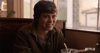 A Young Man Is Sitting At A Table In A Diner With A Drink And Smiling . GIF