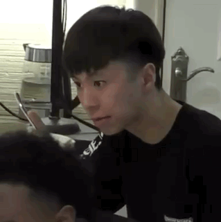 A Young Man Is Sitting At A Table Looking At Another Man 'S Hair . GIF