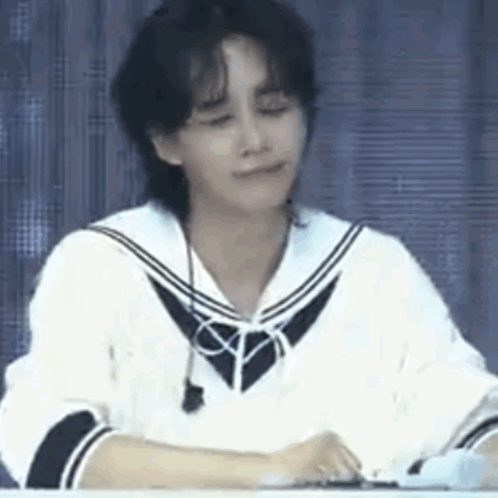 A Young Man Is Sitting At A Table With His Eyes Closed And Wearing A Sailor Uniform . GIF