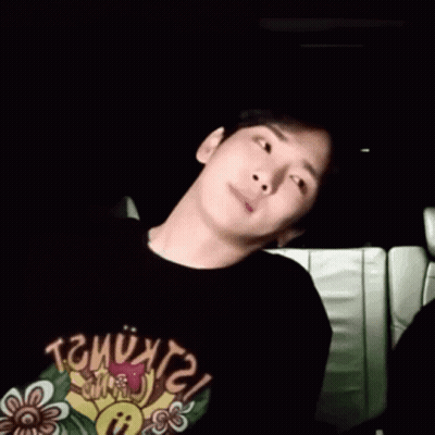 A Young Man Is Sitting In A Car Wearing A Black T-Shirt With A Flower On It . GIF