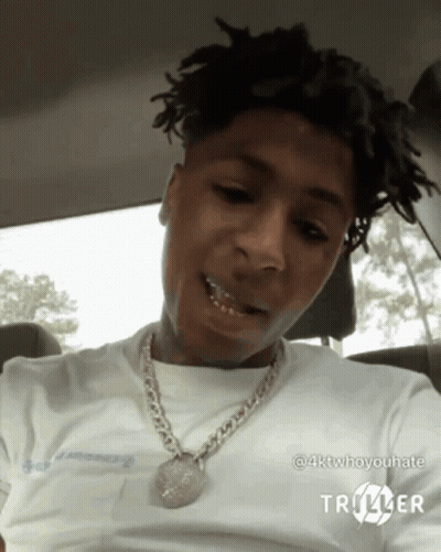 A Young Man Is Sitting In A Car Wearing A White Shirt And A Chain . GIF