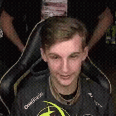 A Young Man Is Sitting In A Chair And Smiling While Wearing A Oneblade Shirt . GIF