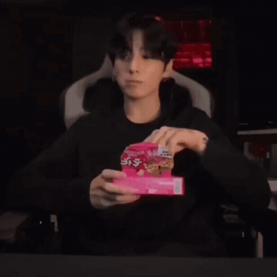 A Young Man Is Sitting In A Chair Holding A Box Of Cookies In His Hands . GIF