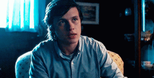 A Young Man Is Sitting In A Chair In A Dark Room Looking At The Camera . GIF
