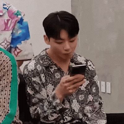 A Young Man Is Sitting In A Chair Looking At His Cell Phone . GIF
