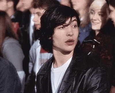 A Young Man Is Sitting In A Crowd Of People Wearing A Leather Jacket . GIF