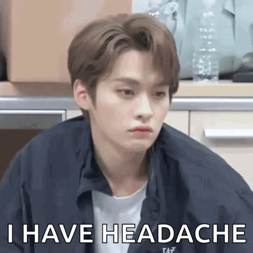 A Young Man Is Sitting In A Kitchen And Making A Funny Face And Saying `` I Have Headache '' . GIF