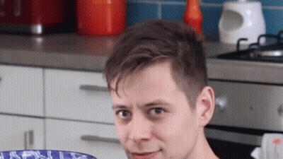 A Young Man Is Sitting In A Kitchen Holding A Bowl Of Food . GIF