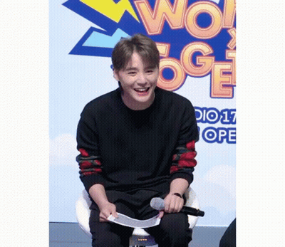A Young Man Is Sitting In Front Of A Sign That Says Wow Oge GIF