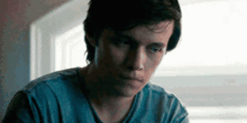 A Young Man Is Sitting In Front Of A Window Wearing A Blue Shirt . GIF