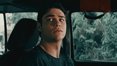 A Young Man Is Sitting In The Back Seat Of A Car Looking At The Camera . GIF