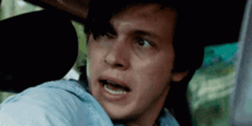 A Young Man Is Sitting In The Back Seat Of A Car With His Mouth Open . GIF