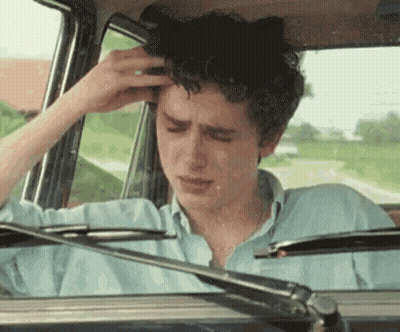 A Young Man Is Sitting In The Driver 'S Seat Of A Car Holding His Head . GIF