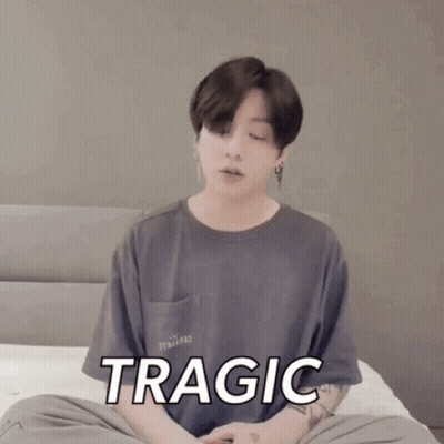 A Young Man Is Sitting On A Bed With His Eyes Closed And The Word Tragic On His Shirt GIF