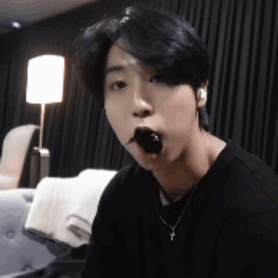 A Young Man Is Sitting On A Couch Eating A Piece Of Chocolate . GIF