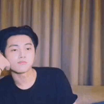 A Young Man Is Sitting On A Couch In Front Of A Window . GIF