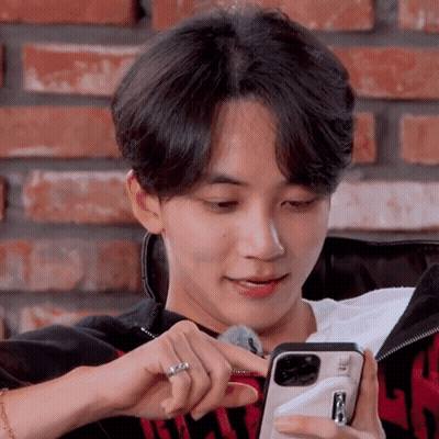 A Young Man Is Sitting On A Couch Looking At A Cell Phone GIF