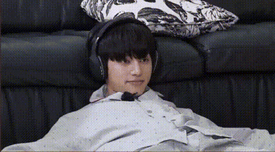 A Young Man Is Sitting On A Couch Wearing Headphones And A Poncho . GIF